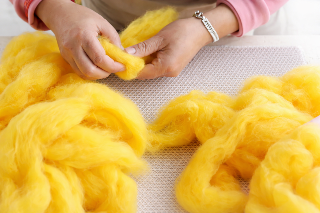 Close-up of vibrant yellow dyed New Zealand wool being hand-sorted by an artisan in Nepal for HillYarn cat caves