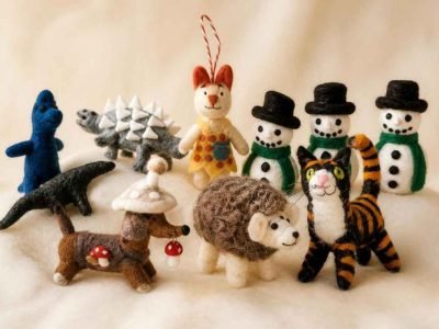 Collection of colorful handmade felt animal toys including a cat, hedgehog, dinosaur, and snowman figures on a soft background.